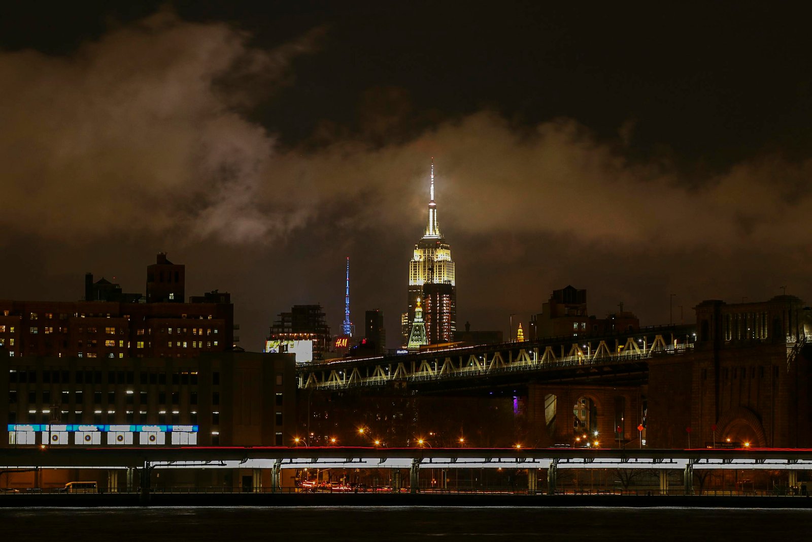 Captivating night view of the Empire State Building illuminated above the Brooklyn Bridge in New York City.