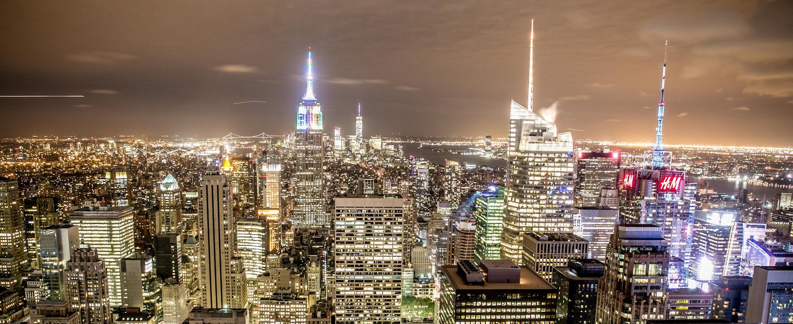 Elevated view of New York City skyline with illuminated skyscrapers and Empire State Building at night.