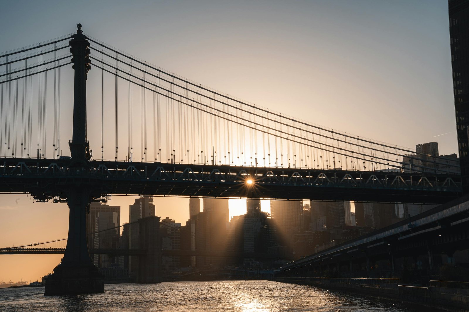 Epic view of sunset through Manhattan Bridge against New York skyline, creating a silhouette of iconic architecture.